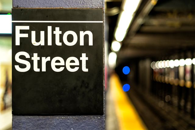 A sign saying "Fulton Street" on a column on a train platform